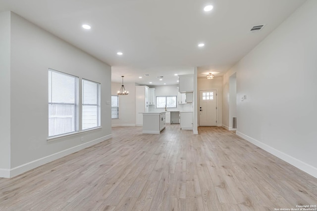 unfurnished living room with recessed lighting, baseboards, light wood finished floors, and an inviting chandelier