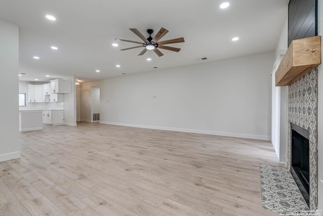 unfurnished living room with ceiling fan, light wood finished floors, a tiled fireplace, and visible vents