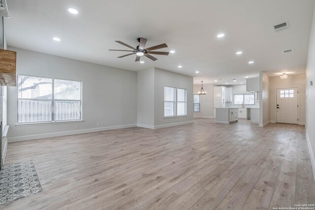 unfurnished living room with recessed lighting, visible vents, light wood-style flooring, and ceiling fan with notable chandelier