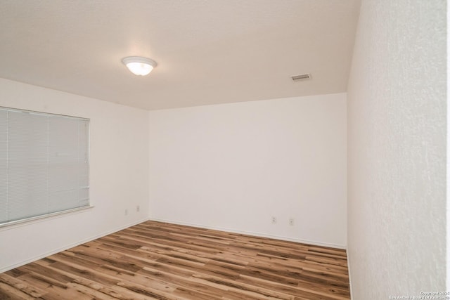 spare room with baseboards, visible vents, and wood finished floors