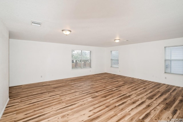 unfurnished room featuring light wood-type flooring, visible vents, and a textured ceiling