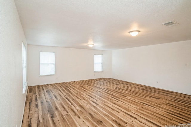 unfurnished room featuring light wood-type flooring, baseboards, visible vents, and a textured ceiling