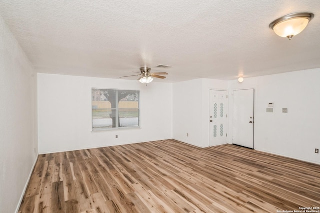 empty room featuring a ceiling fan, visible vents, a textured ceiling, and wood finished floors