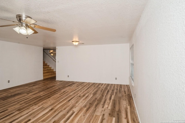 unfurnished living room featuring a textured ceiling, ceiling fan, stairs, and dark wood-type flooring