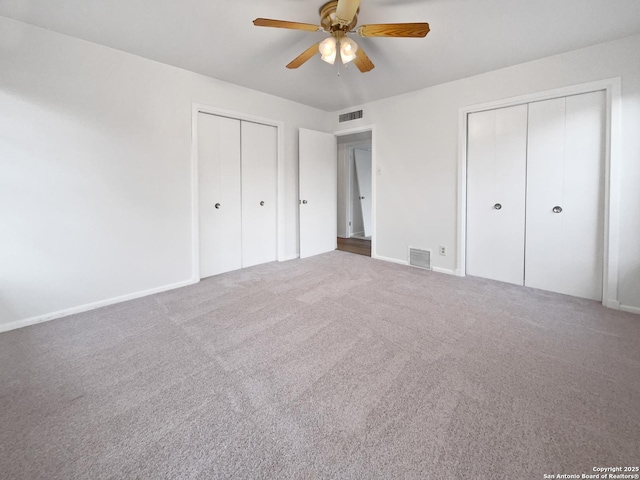 unfurnished bedroom featuring carpet floors, a ceiling fan, visible vents, and two closets