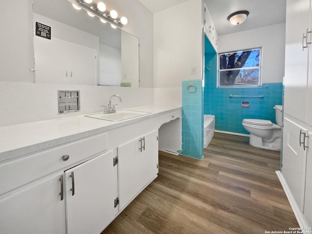 bathroom featuring toilet, a wainscoted wall, wood finished floors, vanity, and tile walls