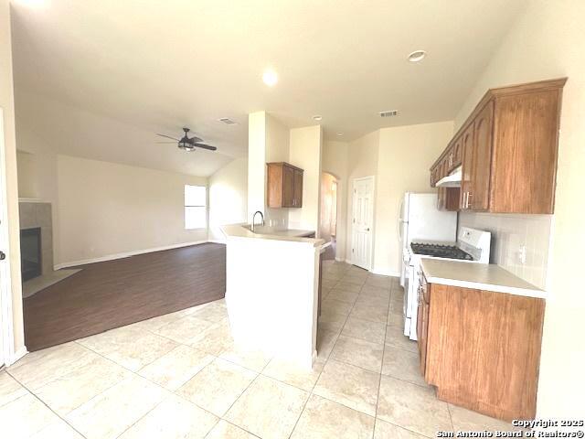 kitchen with brown cabinets, light countertops, open floor plan, white range with gas stovetop, and a peninsula