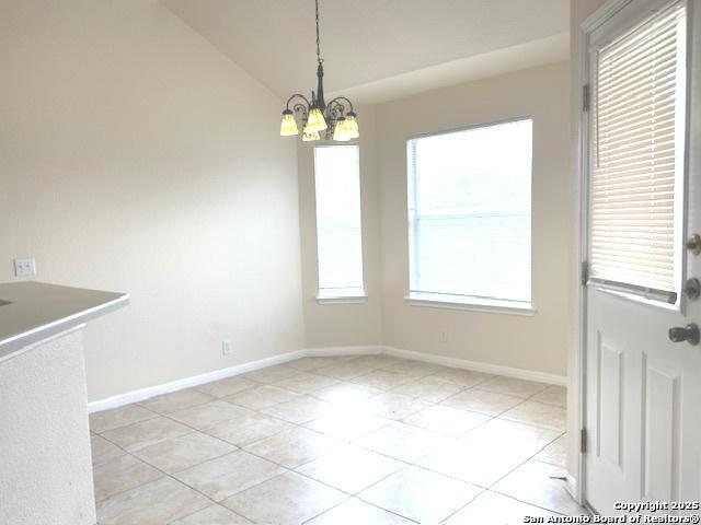 unfurnished dining area with lofted ceiling, an inviting chandelier, and baseboards