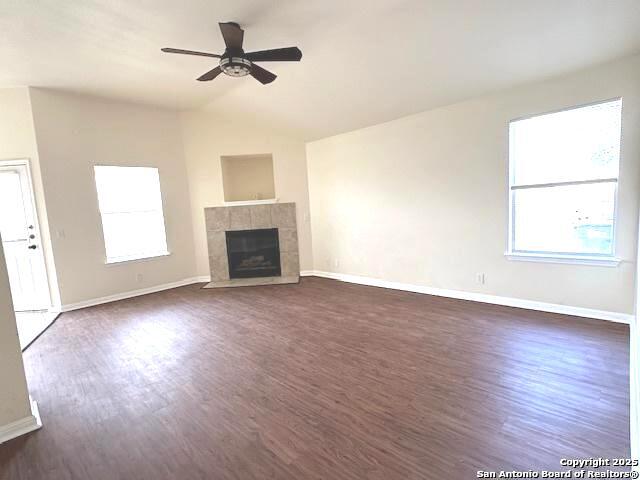 unfurnished living room with a healthy amount of sunlight, dark wood-type flooring, and a tiled fireplace