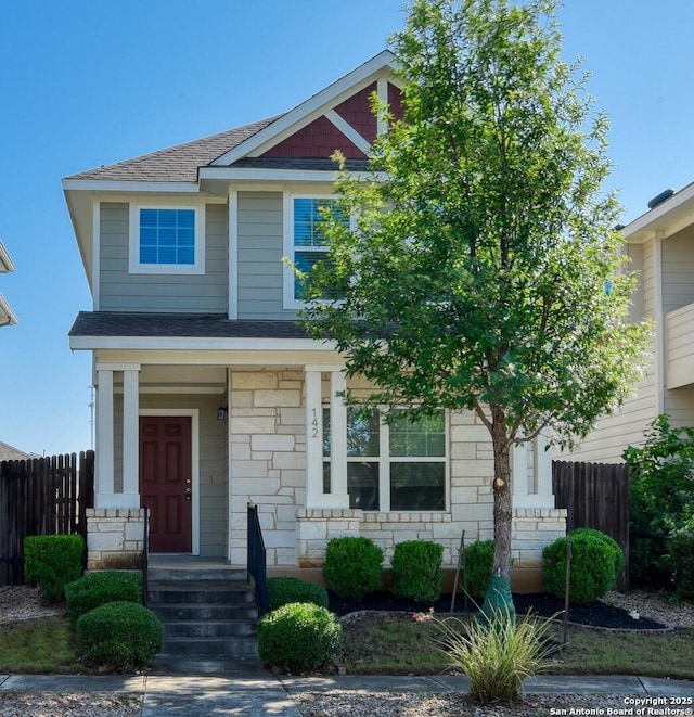 craftsman-style house with stone siding, a shingled roof, and fence