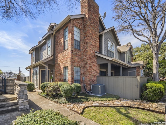 view of home's exterior with a chimney, cooling unit, and brick siding