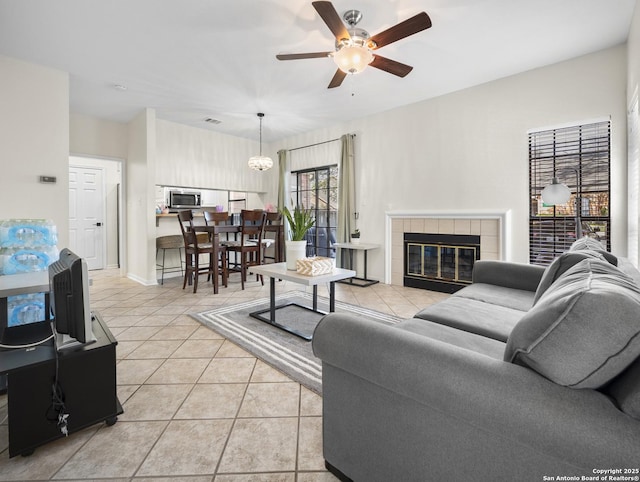 living area featuring visible vents, a tiled fireplace, a ceiling fan, light tile patterned flooring, and baseboards