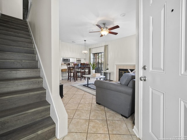 living area with ceiling fan, stairs, a tiled fireplace, and light tile patterned flooring