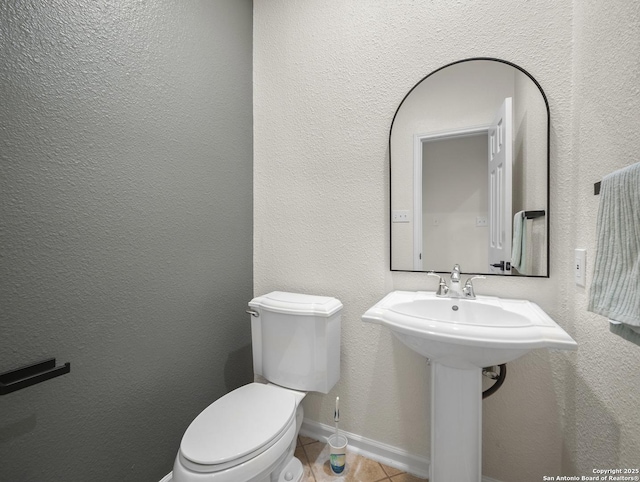 bathroom featuring toilet, tile patterned flooring, baseboards, and a textured wall