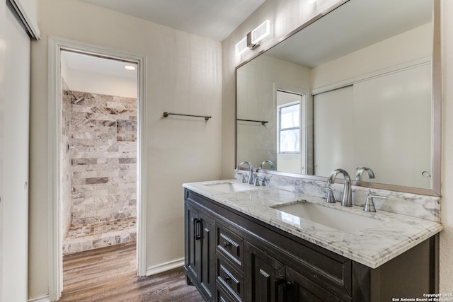 full bathroom with double vanity, a tile shower, a sink, and wood finished floors