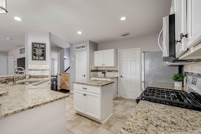 kitchen with visible vents, white cabinets, light stone counters, a center island, and a sink