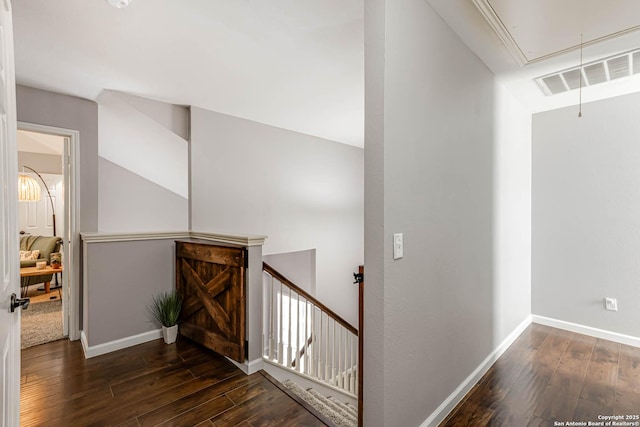 hallway with attic access, visible vents, dark wood-type flooring, and an upstairs landing