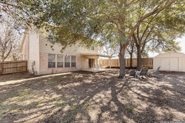 rear view of house with a storage shed, a patio, a fenced backyard, an outbuilding, and brick siding