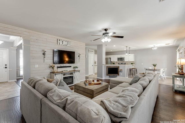 living area featuring baseboards, ceiling fan, dark wood finished floors, and wooden walls