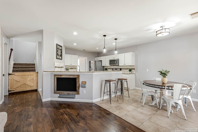 kitchen with decorative backsplash, appliances with stainless steel finishes, a kitchen breakfast bar, a peninsula, and white cabinetry