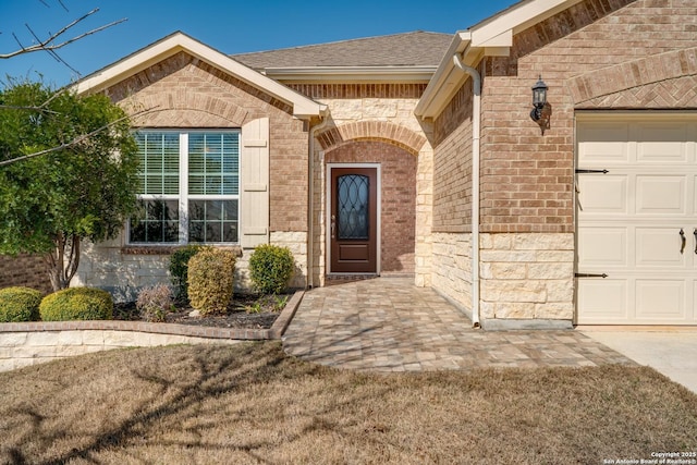 property entrance featuring brick siding, roof with shingles, and an attached garage