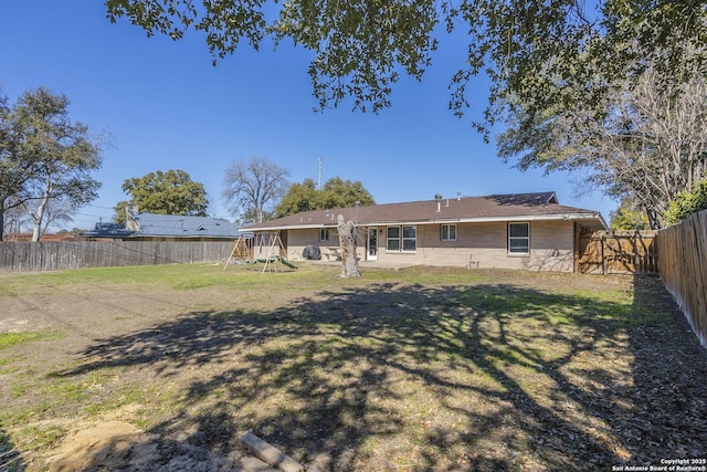 rear view of property with a fenced backyard, a lawn, and a playground