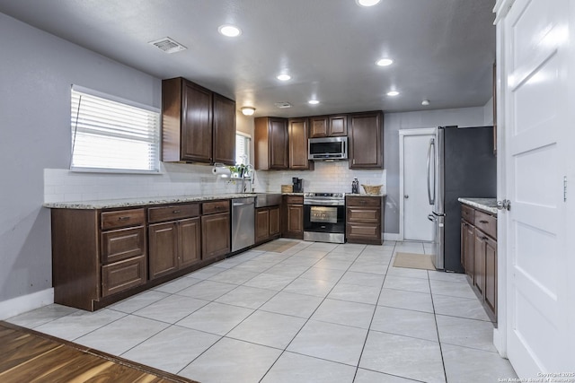 kitchen with appliances with stainless steel finishes, light stone countertops, visible vents, and tasteful backsplash