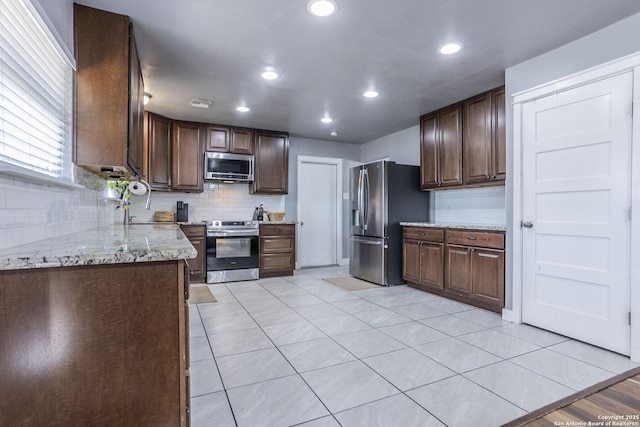 kitchen with stainless steel appliances, dark brown cabinetry, backsplash, and light stone counters