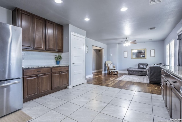 kitchen featuring light tile patterned floors, open floor plan, freestanding refrigerator, dark brown cabinets, and backsplash