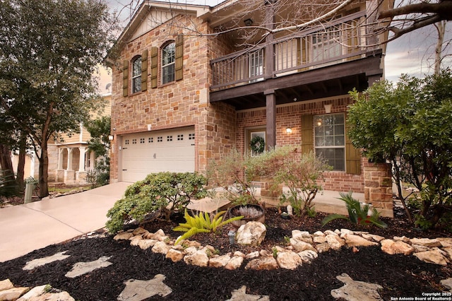 view of front of home with brick siding, concrete driveway, an attached garage, a balcony, and stone siding