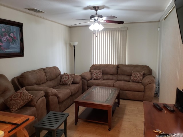 living room with light wood-style flooring, visible vents, ornamental molding, and ceiling fan