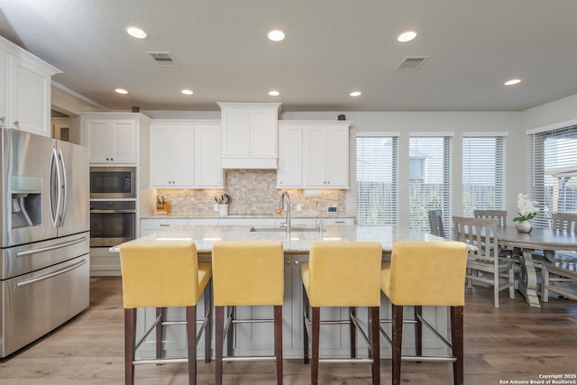 kitchen with white cabinets, a center island with sink, stainless steel appliances, and a sink