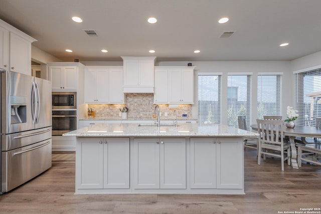 kitchen featuring visible vents, appliances with stainless steel finishes, white cabinets, a sink, and an island with sink