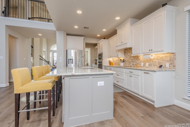 kitchen with a center island with sink, appliances with stainless steel finishes, white cabinetry, a sink, and light stone countertops