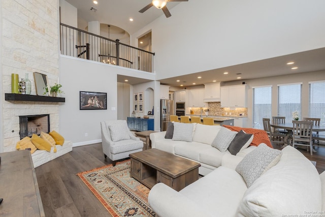 living area featuring arched walkways, a stone fireplace, visible vents, baseboards, and dark wood-style floors