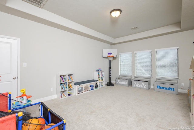 recreation room with carpet floors, a tray ceiling, visible vents, and baseboards