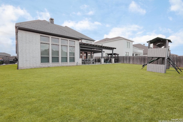 back of house with brick siding, a playground, a shingled roof, a lawn, and fence