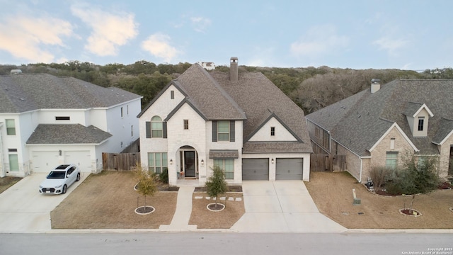 french provincial home featuring a residential view, roof with shingles, driveway, and fence