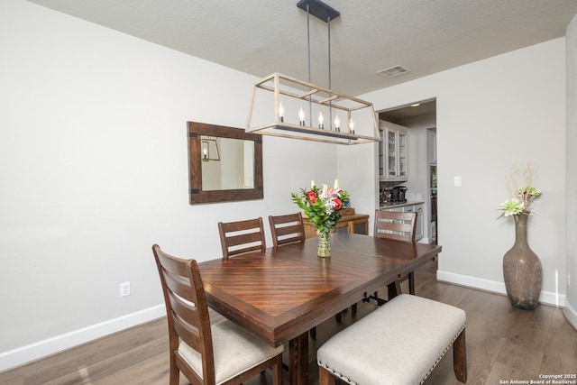 dining space featuring a textured ceiling, wood finished floors, visible vents, and baseboards