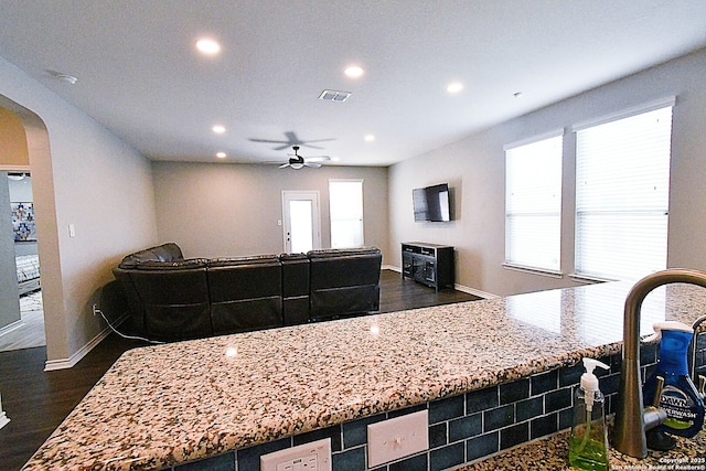 kitchen with dark wood-style floors, arched walkways, light stone counters, recessed lighting, and open floor plan