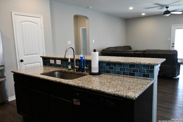 kitchen with open floor plan, a kitchen island with sink, a sink, dark cabinets, and dishwasher