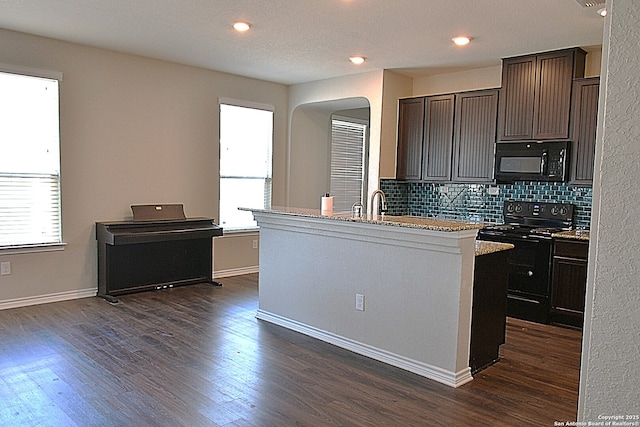 kitchen with dark wood-style flooring, dark brown cabinets, backsplash, black appliances, and an island with sink