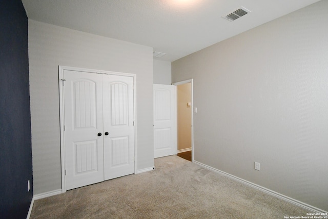 unfurnished bedroom featuring baseboards, a closet, visible vents, and light colored carpet