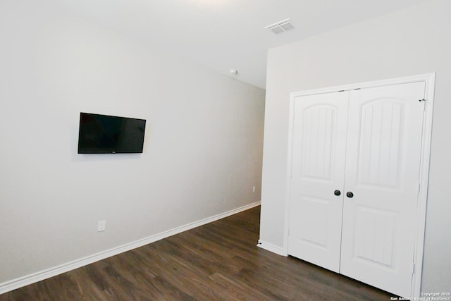 unfurnished bedroom with dark wood-style flooring, a closet, visible vents, and baseboards