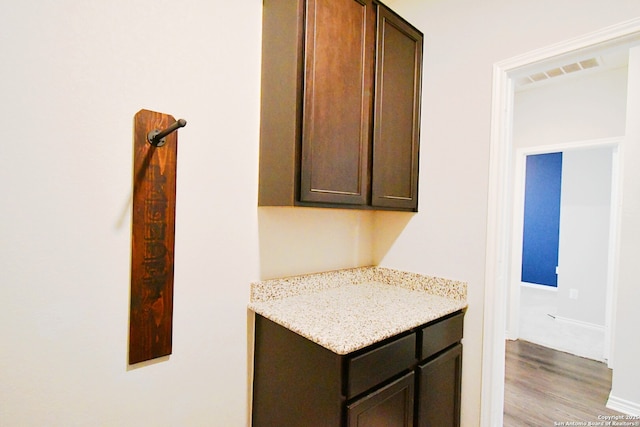 kitchen with visible vents, light stone counters, light wood-style flooring, and dark brown cabinetry