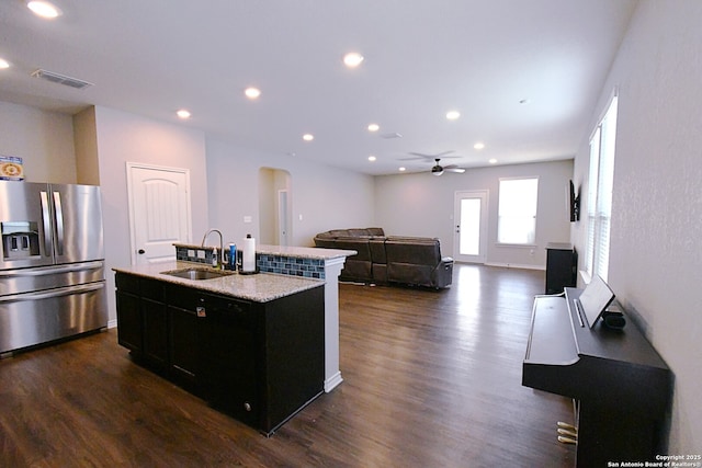 kitchen with stainless steel fridge, a center island with sink, visible vents, arched walkways, and a sink