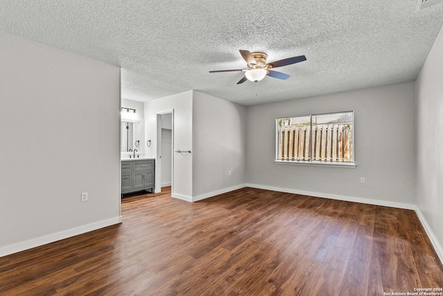 unfurnished bedroom featuring a textured ceiling, baseboards, dark wood-style flooring, and a sink