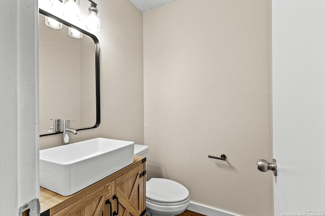 bathroom with toilet, a textured wall, baseboards, and vanity