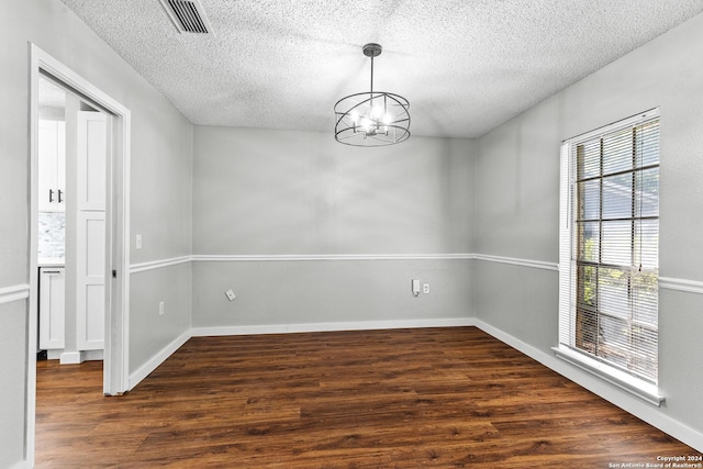 empty room featuring a textured ceiling, visible vents, dark wood finished floors, and a notable chandelier