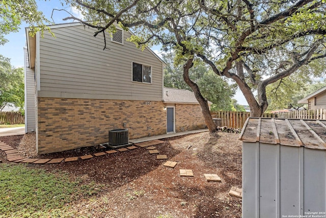 view of side of property featuring fence, an outdoor structure, central AC, and brick siding